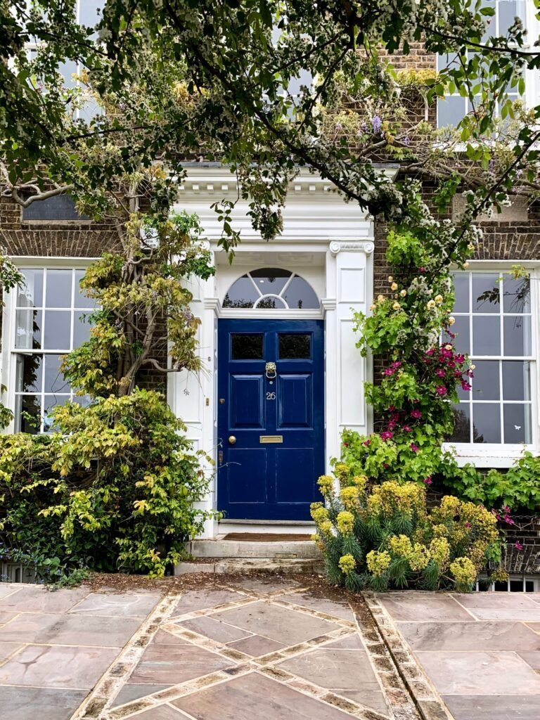 Facade of old English house with blue door and white columns and front garden. Old Georgian house
